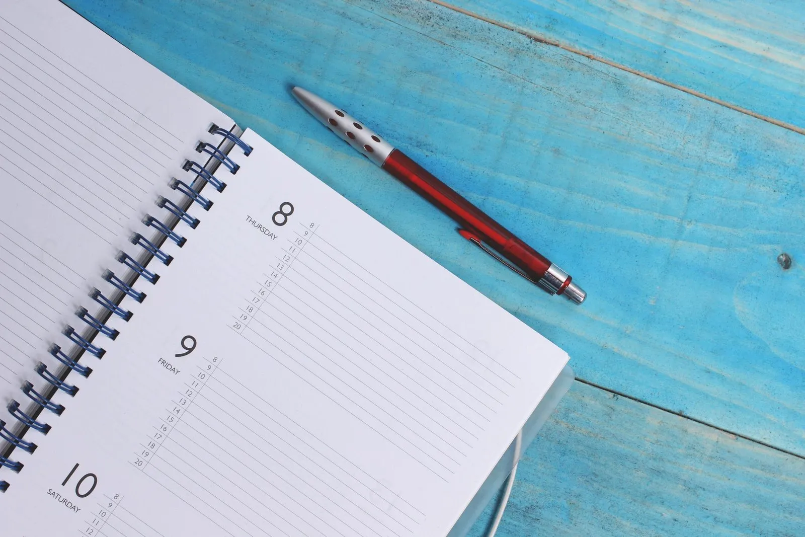 A spiral notebook and a pen on a turquoise wooden table.