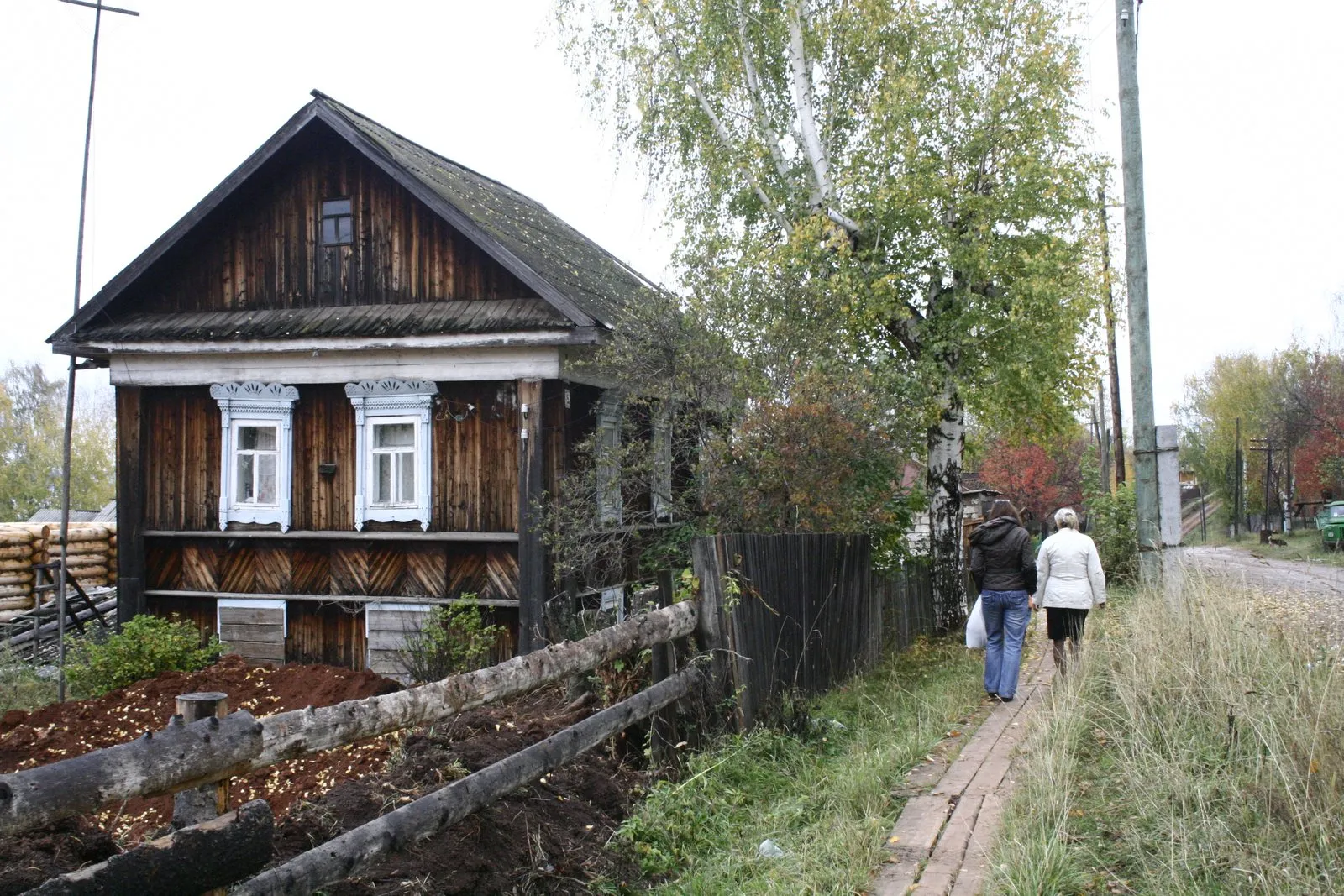 A wooden village house in Russia with people walking along a boardwalk path.